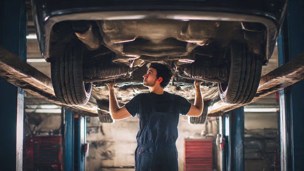 Mechanic inspecting rear differential and wheel bearings under car lifted on jack stands in automotive repair shop