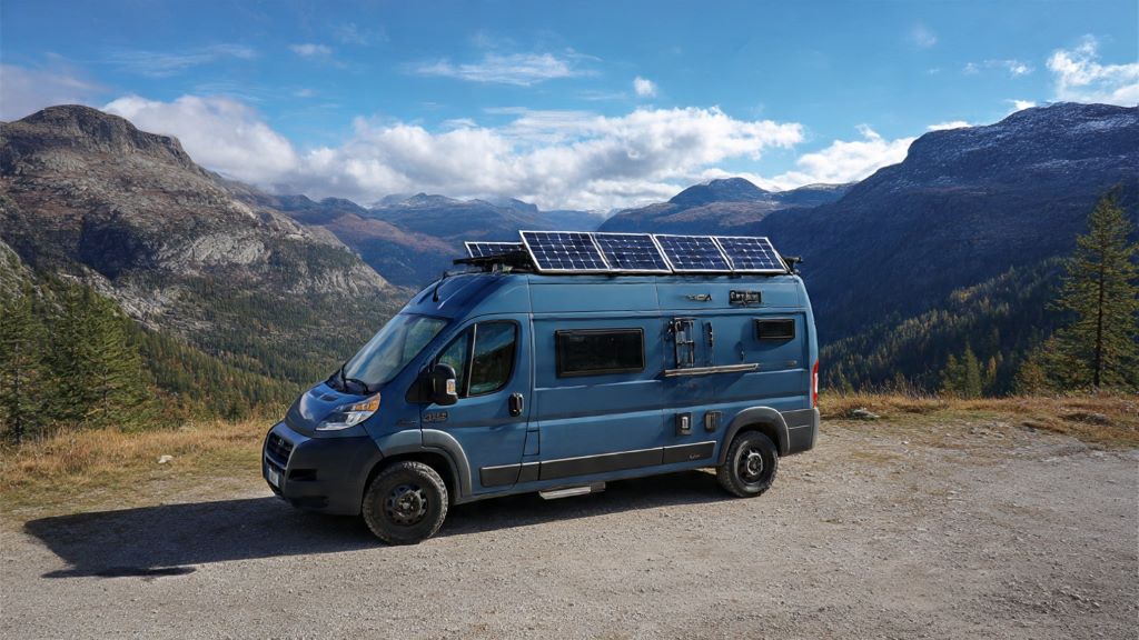 Custom converted campervan with solar panels and roof rack parked in mountain landscape showing self-build modifications