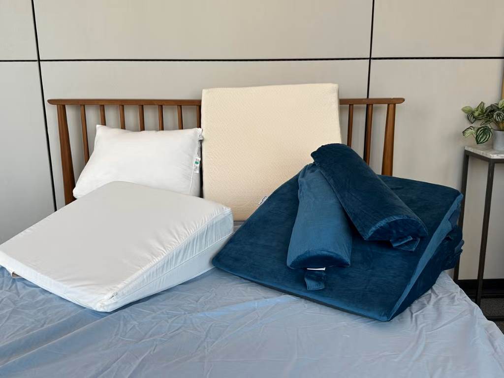Close-up of a foam bed wedge pillow elevating a sleeper's torso for GERD relief at night.