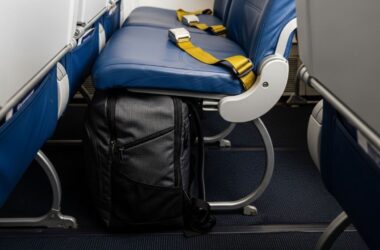 A compact travel backpack placed under an airplane seat, showing it fits within personal item size limits