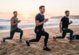 Three men exercising on a sandy beach wearing athletic leggings with side pockets.