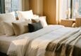 Hands smoothing high thread count white cotton sheets on a mattress.