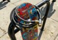 A colorful skateboard secured to a metal rack with a cable lock.