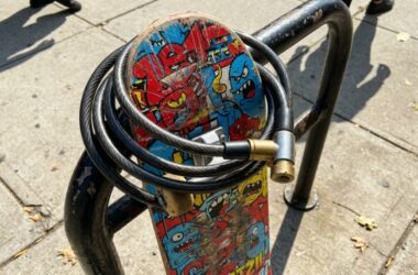 A colorful skateboard secured to a metal rack with a cable lock.